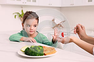 Mother feeding her daughter in kitchen, closeup. Little girl refusing to eat vegetables