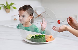 Mother feeding her daughter in kitchen, closeup. Little girl refusing to eat vegetables