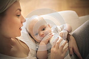 Mother feeding her little baby with milk at home.