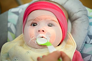 Mother feeding hungry five month old baby with spoon, solid food. Newborn feeding concept