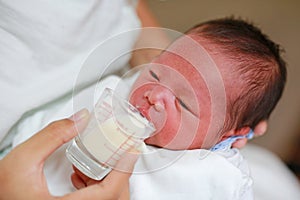 Mother feeding milk infant baby by glass cup