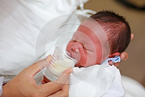 Mother feeding milk infant baby by glass cup