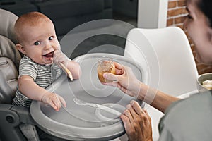 Mother feeding with vegetables or fruits pure baby on highchair