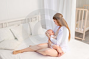 Mother feeds baby 6 months of breast sitting on a white bed at home, place for text