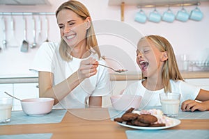 Mother feeds her beautiful daughter with chocolate flakes and laughs loudly. have a good time together, dressed alike