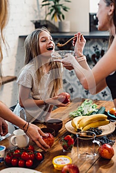 Mother feeds her daughter with a spoon jokingly.