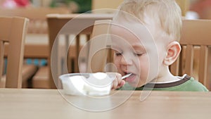 Mother feeds her young son with ice cream from a spoon. They are sitting in a street cafe. The boy really likes the