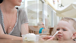 Mother feeds her young son with ice cream from a spoon. They are sitting in a street cafe. The boy really likes the