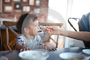 Mother feeds a hungry baby boy with soup in a restaurant