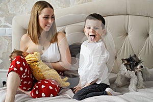 the mother feeds the newborn baby breast milk on the bed with elder brother