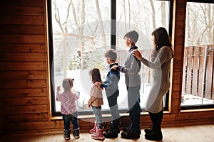 Mother and four kids in modern wooden house against large window