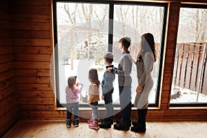 Mother and four kids in modern wooden house against large window