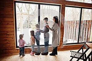 Mother and four kids in modern wooden house against large window