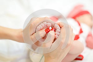 Mother gentle hands with red nails holding newborn baby legs.