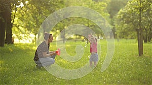 Mother and girl blowing soap bubbles outdoor. Parent and kid having fun in park.