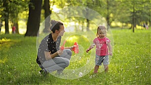 Mother and girl blowing soap bubbles outdoor. Parent and kid having fun in park.