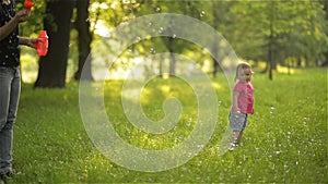 Mother and girl blowing soap bubbles outdoor. Parent and kid having fun in park.