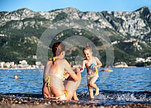 Mother and girl child playing on sandy beach with sea at background. Becici, Montenegro