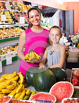 Mother with girl picking bananas on market