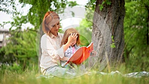 Mother and girl sit under a tree reading a book