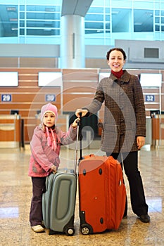 Mother and girl with suitcases standing at airport