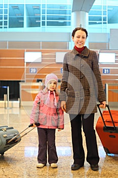 Mother and girl with suitcases standing at airport