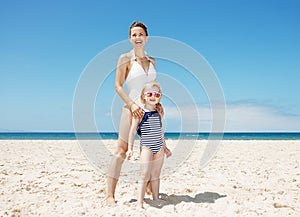 Mother and girl in swimsuits at sandy beach on a sunny day