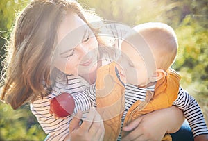 Mother give to child (baby boy) ripe red apple in the sunny autumn (fall) day. Kid eating healthy food, snack.