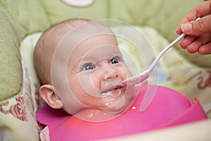 Mother gives baby food from a baby spoon. Smiling baby eating food first time. weaning baby