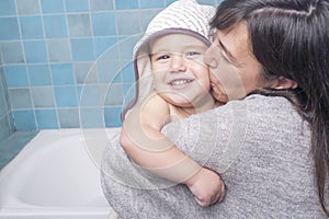 Mother gives a big hug and a kiss to her son while toweling him off after bath time