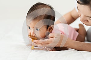 mother gives a pacifier to her infant baby girl on bed