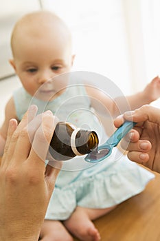 Mother giving baby medicine indoors