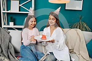 Mother giving birthday cake to funny little girl at home