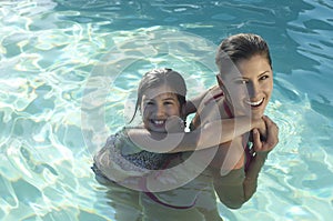 Mother Giving Daughter Piggy Back In Swimming Pool