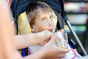 Mother giving disabled child a drink. Cute little girl sitting in wheelchair. Child cerebral palsy. Disability. Inclusion