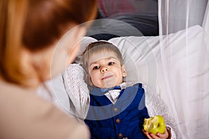 Mother giving good night kiss to sleeping son. Mom putting son to bed