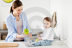 Mother giving green apple to baby at home kitchen