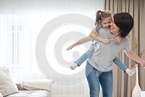 Mother giving joyful piggyback ride to her daughter, having fun at home, single mother happy family concept