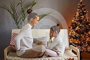 Mother giving present box to her little daughter, smiling girl covering her eyes and waiting her gift, family posing near