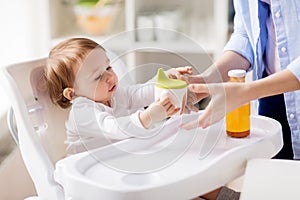 Mother giving spout cup with juice to baby at home