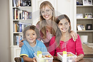 Mother Giving Two Children Healthy Lunchboxes In Kitchen