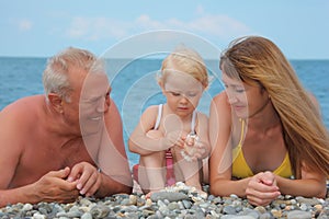 Mother and grandfather with child lie on sea coast