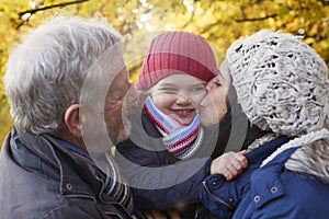 Mother And Grandfather Cuddle Girl On Autumn Walk