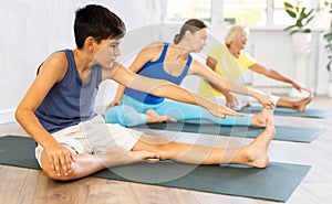 Mother, grandmother and adolescence son do exercise Janu Shirshasana pose.