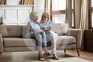 Mother and grownup daughter sitting on couch using computer