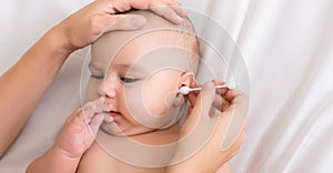 Mother hand cleaning baby ear with cotton swab