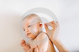 Mother hand cleaning baby ear with cotton swab