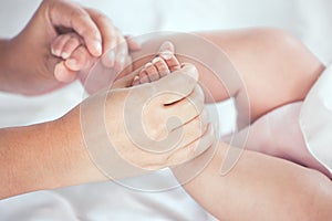 Mother hand holding little baby girl feet while she lying on bed