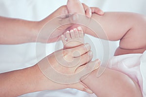 Mother hand holding little baby girl feet while she lying on bed