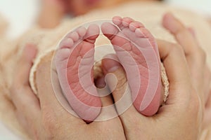 Mother hand holding newborn baby feet on bed